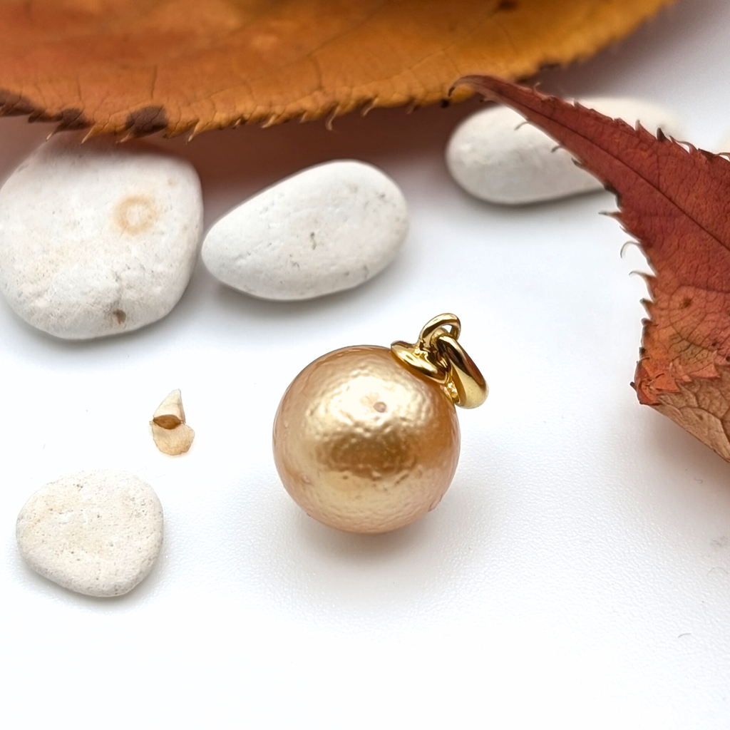 Gold south sea pearl pendant on a white surface with leaves and stones