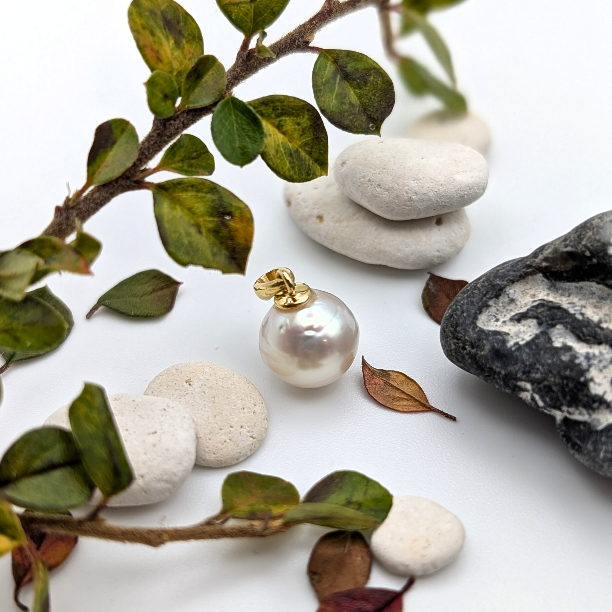 South sea Pearl pendant with gold vermeil bail on a white surface with stones and leaves